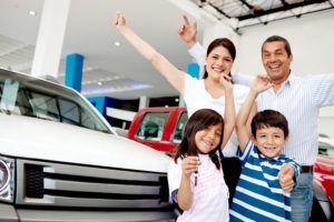 Happy family at a car dealership with arms up celebrating having a new car