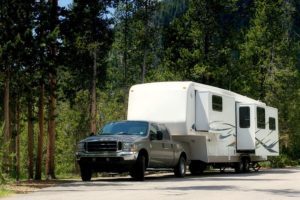 A pickup truck hitched to a large RV camper trailer in a wooded park